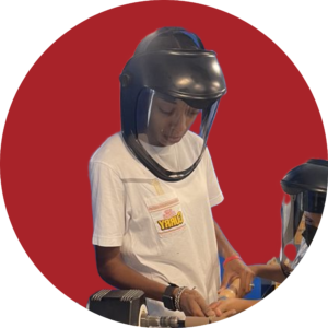 A Black woman with a welder's mask helping a child use an industrial machine